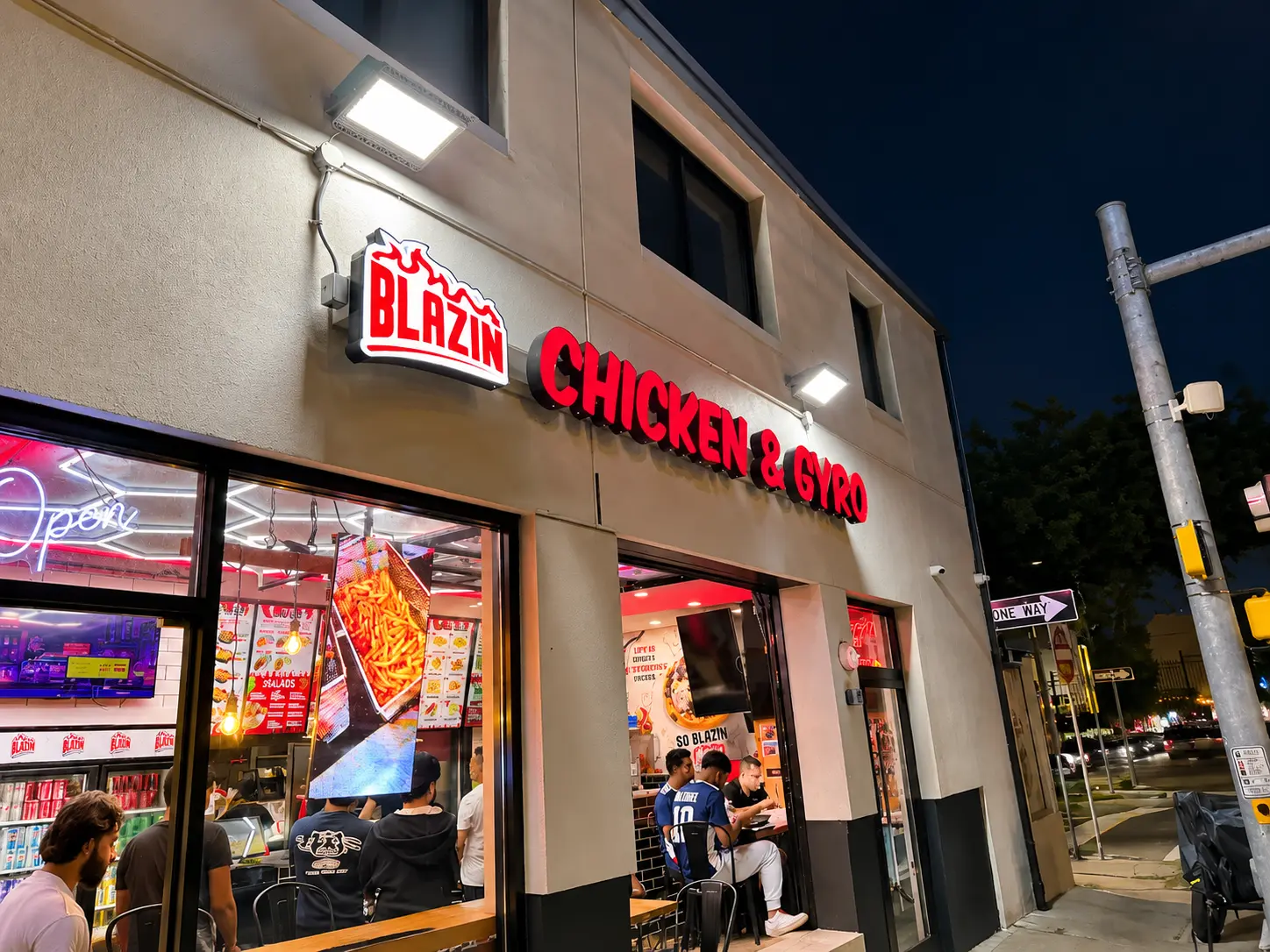 Blazin Chicken & Gyro storefront at night on East Broadway in Hackensack NJ, with the red Chicken & Gyro sign lit up and customers eating inside